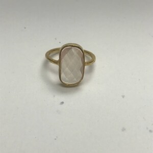May include: A gold ring with a rectangular, faceted, light pink gemstone.