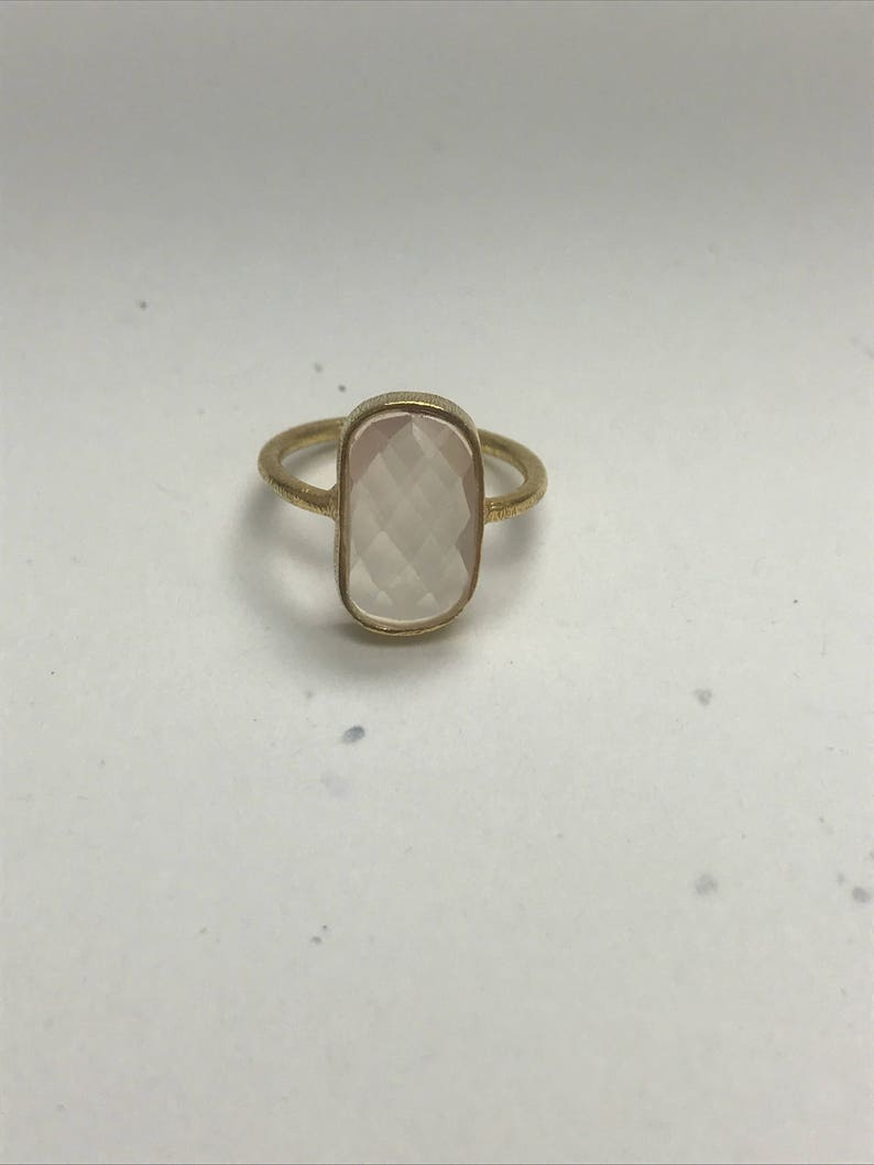 May include: A gold ring with a rectangular, faceted, light pink gemstone.