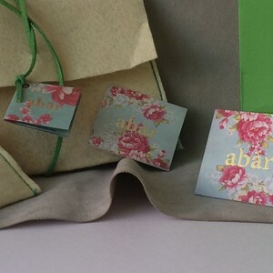 K&ouml;nnte beinhalten: Vier kleine, cremefarbene Filztaschen mit gr&uuml;nen Schleifenb&auml;ndern und floralen Geschenkanh&auml;ngern. Die Anh&auml;nger haben den Text "abar" und "www.loveabar.com".