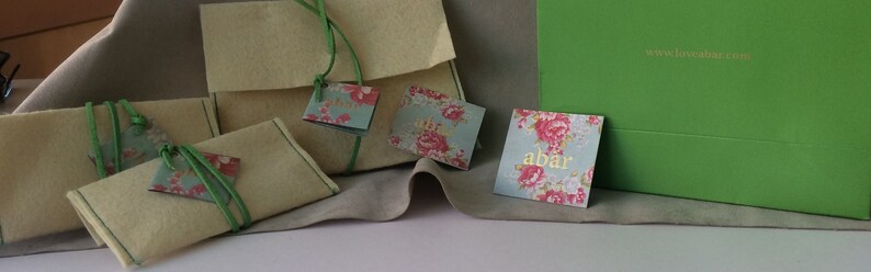 K&ouml;nnte beinhalten: Vier kleine, cremefarbene Filztaschen mit gr&uuml;nen Schleifenb&auml;ndern und floralen Geschenkanh&auml;ngern. Die Anh&auml;nger haben den Text "abar" und "www.loveabar.com".
