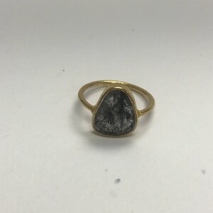 May include: A gold ring with a clear, faceted gemstone set in a triangular shape. The gemstone has black inclusions.
