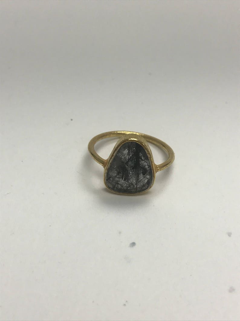 May include: A gold ring with a clear, faceted gemstone set in a triangular shape. The gemstone has black inclusions.