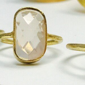 May include: Three gold rings with different gemstone settings. The first ring has a light blue oval-shaped gemstone. The second ring has a clear oval-shaped gemstone. The third ring has a dark gray, almost black, oval-shaped gemstone.