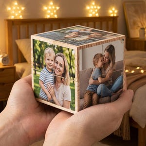 Könnte beinhalten: Ein Holz-Fotowürfel mit Familienfotos. Der Würfel, gehalten in den Händen einer Person, zeigt Bilder einer Mutter und eines Kindes. Der Würfel ist aus hellem Holz mit natürlicher Oberfläche gefertigt.