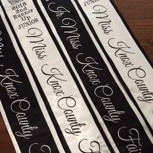 May include: Three black and white sashes with the text "Miss Knox County Fair" and "Jr. Miss Knox County Fair" and "2018 1st Runner Up Junior" and "2018 2nd Runner Up Junior".