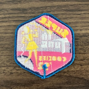 May include: A pink and white embroidered patch with a blue border. The patch features a cartoon girl holding a phone and the text "Betty's Beauty Shop".