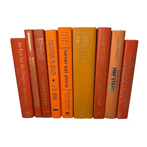 May include: A collection of hardcover books in shades of orange and yellow, arranged upright. Titles include "An Eye for the Dragon," "Salvation in Death," and "The Lake House." The spines display author names and book titles.
