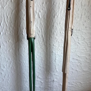 May include: Two carved wooden figures of men. One figure wears a red fez, a cream-colored jacket, and green pants. The other figure wears a white cap and a cream-colored jacket. Both figures stand on black square bases.