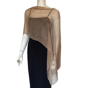 May include: A sheer, shimmering, gold-toned shawl draped over a black dress on a mannequin. The shawl has a flowing, asymmetrical design, adding a touch of elegance. The dress is a simple, sleeveless style.
