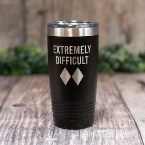 May include: Black stainless steel tumbler with a white inscription that reads "EXTREMELY DIFFICULT" and two black diamond symbols.