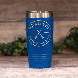 May include: A blue stainless steel tumbler with a white circle design that says "whatever floats your boat" with two crossed oars inside the circle.