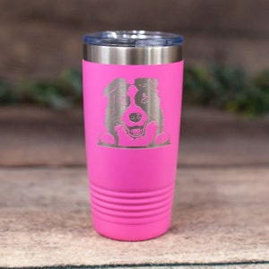 May include: A pink stainless steel tumbler with a laser-etched design of a Border Collie dog peeking over the top. The tumbler has a double-wall insulated design to keep drinks cold or hot.