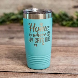 May include: A turquoise stainless steel tumbler with a white inscription that reads "Home is where my cats are" and paw prints.