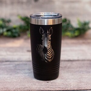 May include: A black stainless steel tumbler with a laser-etched image of a zebra. The tumbler has a black powder-coated finish and a lid.