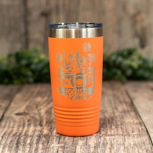 May include: Orange stainless steel tumbler with a camera and flowers design. The text "Focus on the Good" is engraved on the tumbler.