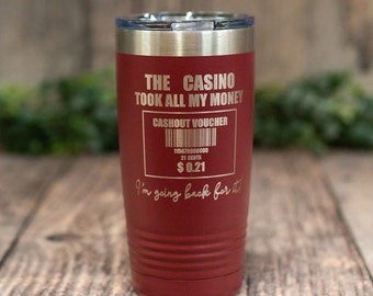 Può includere: Un bicchiere in acciaio inossidabile rosso con una scritta bianca che recita "The Casino Took All My Money" e un finto buono di pagamento del casinò con il testo "Cashout Voucher" e "€ 0,21".