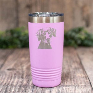 May include: A light purple insulated tumbler with a silver lid. The tumbler features a detailed engraving of a dog's face. The design is centered on the tumbler, which has a ridged texture near the bottom. The tumbler is designed to hold approximately 20 ounces.
