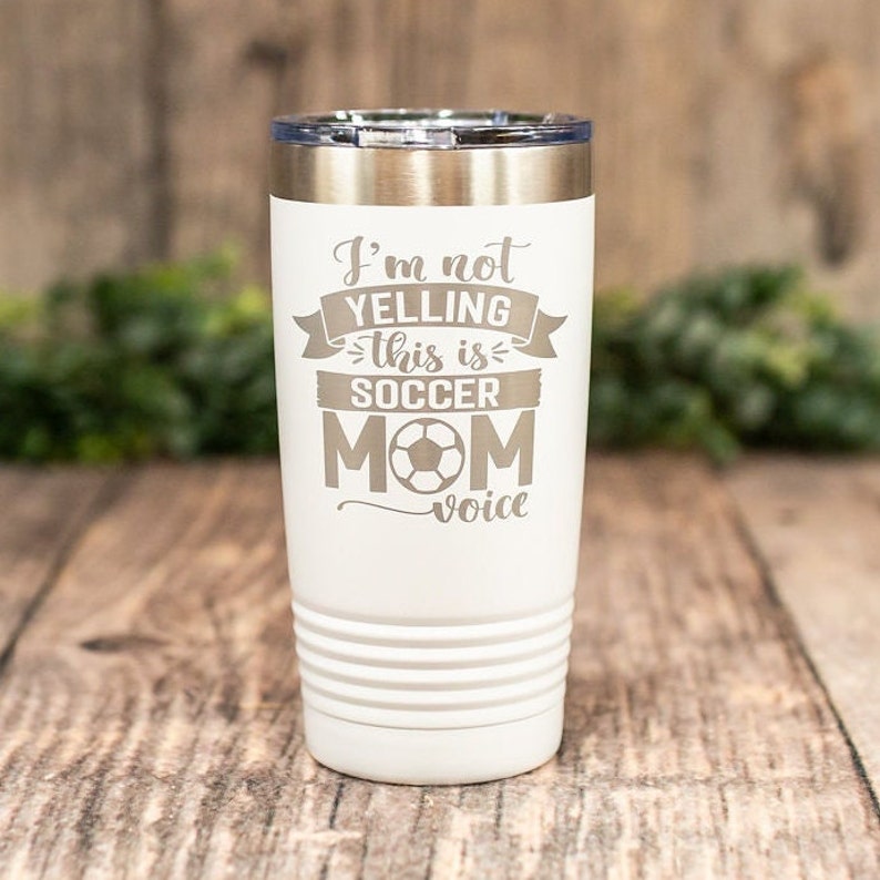 May include: White stainless steel tumbler with a gray engraved design that reads "I'm not yelling this is soccer mom voice" with a soccer ball graphic.
