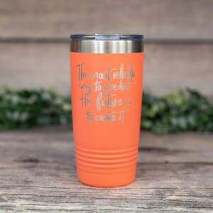 May include: Orange stainless steel tumbler with a silver lid. The tumbler has a quote engraved on the side: "The most reliable way to predict the future is to create it."