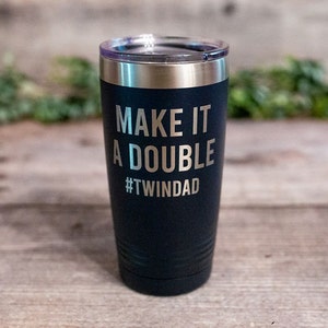 May include: Black insulated tumbler with a silver rim and a clear lid. The text "MAKE IT A DOUBLE #TWINDAD" is etched in silver. The tumbler is cylindrical and appears to be made of stainless steel.