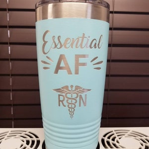 May include: A light blue stainless steel tumbler with a silver lid. The tumbler has the text "Essential AF" and a silver medical symbol with "RN" underneath.