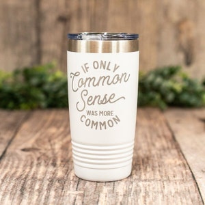 May include: White travel tumbler with a silver lid and the phrase "If Only Common Sense Was More Common" in a script font. The tumbler has a ridged design near the base and is set against a wooden background.