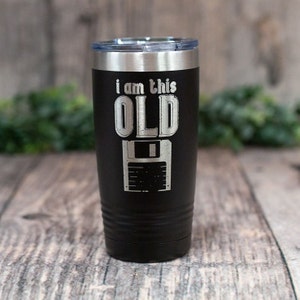 May include: Black stainless steel tumbler with a silver lid. The tumbler has the text "i am this OLD" and a graphic of a floppy disk.