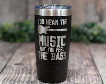 May include: Black stainless steel tumbler with a silver inscription that reads "You hear the music but you feel the bass". A silver electric guitar graphic is above the text.