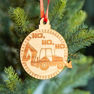 May include: A wooden Christmas ornament shaped like a circle with a red ribbon. The ornament features a cartoon image of a tractor with the text "Ho, Ho, Ho" around the edge.