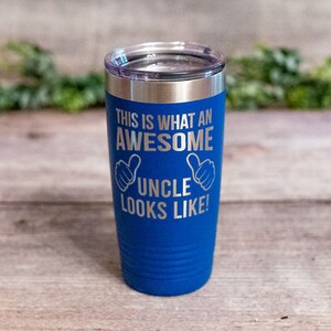 May include: Blue stainless steel tumbler with a silver inscription that reads "This is what an awesome uncle looks like!" with two thumbs up symbols.
