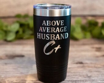 May include: Black insulated tumbler with a silver rim and lid. The tumbler features the text "ABOVE AVERAGE HUSBAND" in silver lettering, along with the initials "C+". The tumbler is designed to keep beverages hot or cold.
