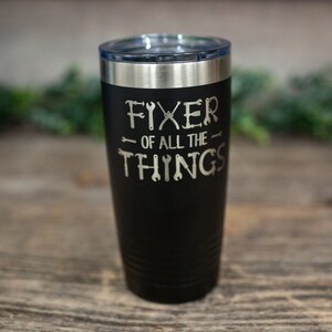 May include: Black stainless steel tumbler with a silver lid. The tumbler has the text "Fixer of all the things" with a graphic of tools around the text.