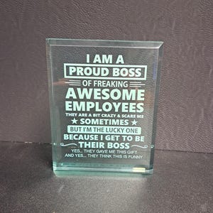 May include: A glass plaque with a white inscription that reads "I am a proud boss of freaking awesome employees. They are a bit crazy & scare me sometimes, but I'm the lucky one because I get to be their boss. Yes... they gave me this gift and yes... they think this is funny."