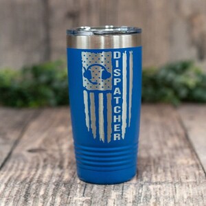 May include: A blue stainless steel tumbler with a silver American flag design and the words "DISPATCHER" engraved on it. The flag has a blue headset with a star inside.