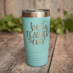 May include: A turquoise stainless steel tumbler with a silver lid. The tumbler has the text "best teacher ever" in silver lettering.