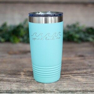 May include: A turquoise stainless steel tumbler with a silver lid. The tumbler has a wave design and the text "spirit lead me" on the front.