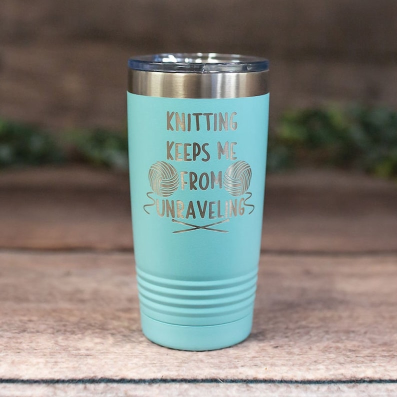 May include: A turquoise stainless steel tumbler with a silver inscription that reads "Knitting keeps me from unraveling" with a graphic of two yarn balls and knitting needles.