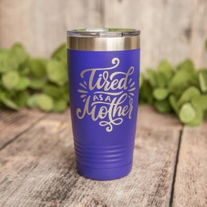 May include: A purple stainless steel tumbler with a silver lid. The tumbler has the text "Tired as a Mother" in a silver script font.