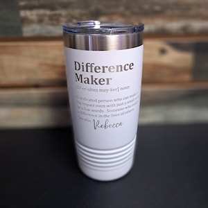 May include: White stainless steel tumbler with a silver lid. The tumbler has a definition of the word "Difference Maker" with the name "Rebecca" at the bottom.