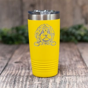 May include: Yellow stainless steel tumbler with a laser engraved image of a dog's head. The dog is looking at the camera with its paws resting on the edge of the tumbler.