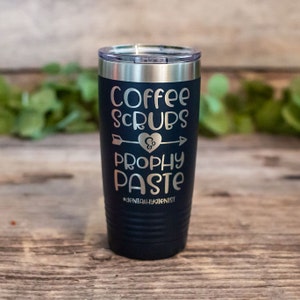 May include: A dark blue stainless steel tumbler with a silver lid. The tumbler has the text "Coffee Scrubs & Prophy Paste #dentalhygienist" printed on it.