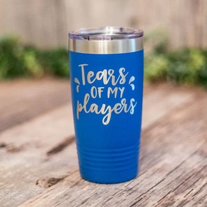 May include: A blue stainless steel tumbler with a silver lid. The tumbler has the text "Tears of my players" engraved on the side.