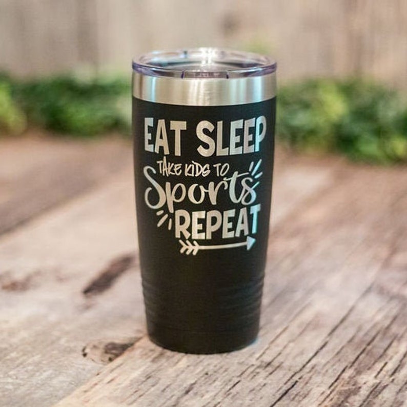 May include: Black stainless steel tumbler with a white inscription that reads "Eat Sleep Take Kids to Sports Repeat" with an arrow pointing to the right.