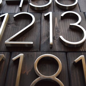 Puede incluir: Primer plano de n&uacute;meros de casa de metal plateado sobre un fondo de madera oscura. Los n&uacute;meros son 1, 2, 3, 7, 8, 10, 11, 12, 13 y 14.