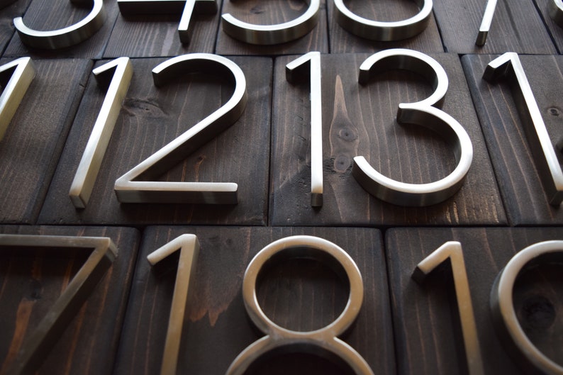 Puede incluir: Primer plano de n&uacute;meros de casa de metal plateado sobre un fondo de madera oscura. Los n&uacute;meros son 1, 2, 3, 7, 8, 10, 11, 12, 13 y 14.