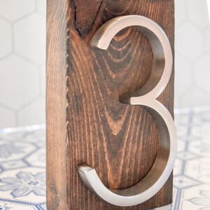 Peut inclure: Un bloc de bois teint&eacute; fonc&eacute; pr&eacute;sente le chiffre 3 argent&eacute;. Le grain du bois est visible, et le chiffre est en m&eacute;tal bross&eacute;. Cette pi&egrave;ce d&eacute;corative convient &agrave; la d&eacute;coration int&eacute;rieure.