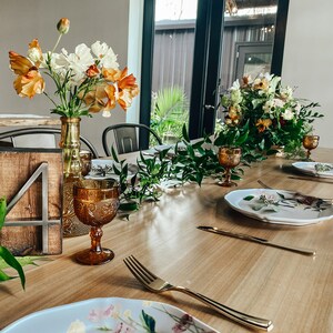 Peut inclure: Une table en bois dress&eacute;e pour une occasion sp&eacute;ciale, avec des compositions florales, de la verrerie ambr&eacute;e et des assiettes d&eacute;coratives. Un num&eacute;ro de table en bois 4 est visible. La table est dress&eacute;e avec des couverts dor&eacute;s et de la verdure.