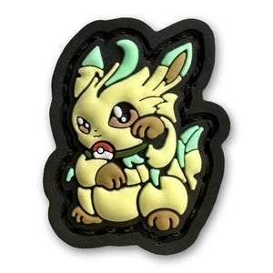 Pode incluir: Um personagem de desenho animado amarelo e verde com uma Poké Ball vermelha. O personagem tem olhos grandes e uma expressão amigável. O personagem é um patch de borracha.