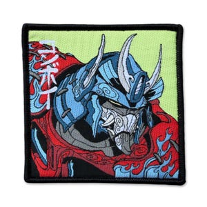 May include: Embroidered patch featuring a detailed illustration of a samurai warrior in a blue and red color scheme. The patch has a black border and a light green background. Japanese text is visible on the left side of the patch.
