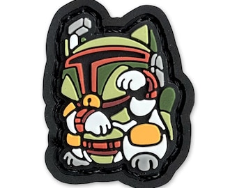 Può includere: Una toppa ricamata nera e verde con un'immagine di cartone animato di Boba Fett di Star Wars. La toppa ha la forma di un gatto e ha un viso bianco con una bocca rossa e occhi gialli.